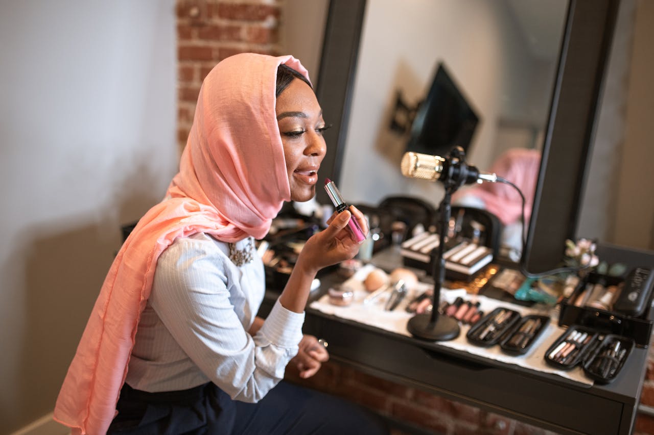 services-01 Muslim woman in pink hijab applying makeup while recording a beauty vlog indoors.