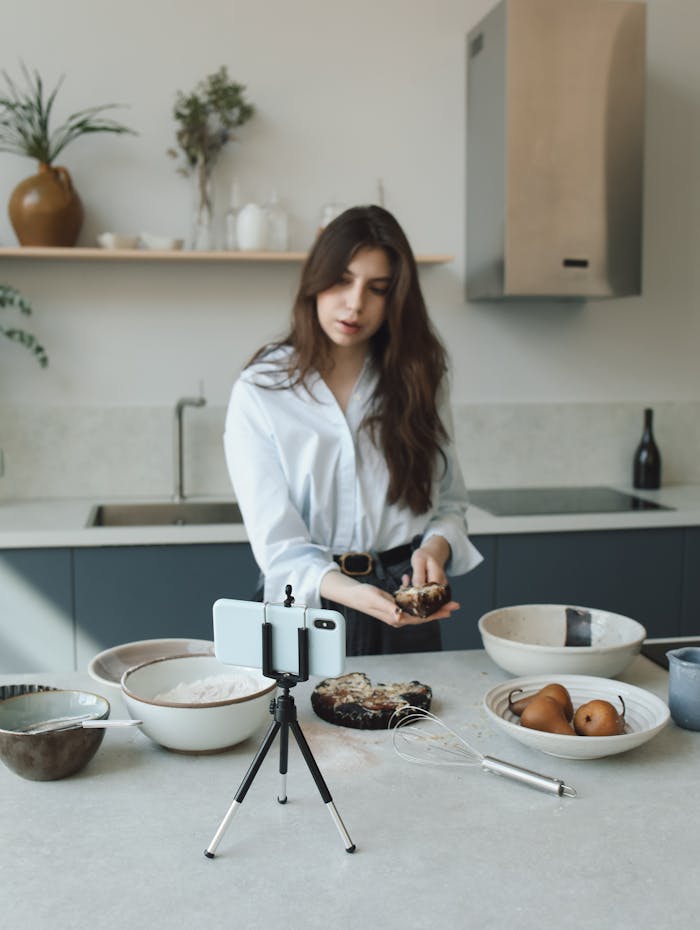 our-story Woman creating a cooking blog video in a modern kitchen with phone on tripod.